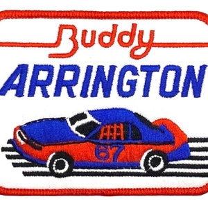 May include: A white embroidered patch with a red border. The patch features a blue and red race car with the number 67 on the side. The text "Buddy Arrington" is above the car in red and blue lettering.