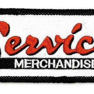 以下が含まれることがあります： 赤い筆記体で「Service」、白いブロック体で「MERCHANDISE」と書かれた刺繍パッチ。パッチは白い背景に黒い縁取りがされています。
