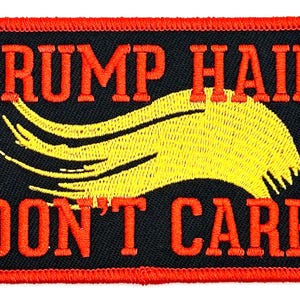 May include: A black embroidered patch with red stitching. The patch features a yellow stylized hair design and the text "TRUMP HAIR DON'T CARE".
