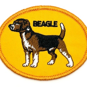 May include: An embroidered yellow oval patch with a brown and black Beagle dog illustration and the word "BEAGLE" in black text.