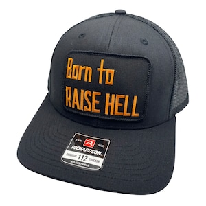Op de afbeelding: Zwarte truckercap met een zwart en oranje patch met de tekst "Born to Raise Hell". De pet is verstelbaar en heeft een Richardson-logo aan de zijkant.