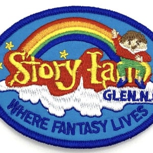 May include: A blue and white embroidered patch with a rainbow, a cloud, and the text "Story Land, Glen, NH, Where Fantasy Lives".