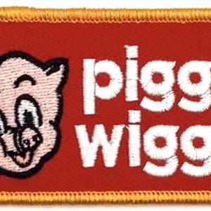 Może przedstawiać: Haftowana naszywka z uśmiechniętą świnią w czapce kucharskiej, z napisem "piggly wiggly" w białych literach na czerwonym tle. Naszywka ma złotą obwódkę.