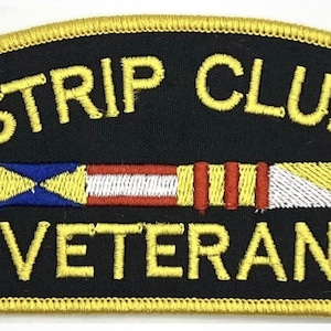 May include: A black embroidered patch with yellow stitching. The patch reads "Strip Club Veteran" with a yellow, red, white, and blue flag design in the middle.