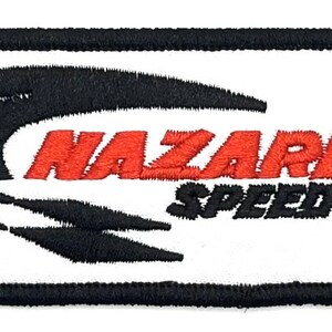 May include: White embroidered patch with black outline. The patch features a black stylized racing track design and the text "Nazareth Speedway" in red.