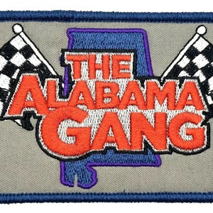 Könnte beinhalten: Ein gestickter Aufnäher mit grauem Hintergrund und blauem Rand. Der Aufnäher zeigt eine violette und blaue Umrandung des Bundesstaates Alabama mit dem Text "THE ALABAMA GANG" in roten und weißen Buchstaben. Zwei karierte Flaggen befinden sich auf beiden Seiten der Staatsumrandung.
