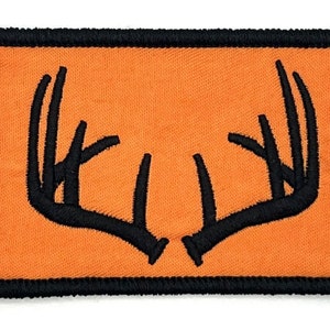 Może przedstawiać: Pomarańczowa łatka z tkaniny z haftowanym czarnym wzorem pary jelenich rogów.