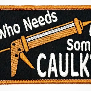 May include: A black and gold embroidered patch with the text "Who Needs Some Caulk?" and a cartoon image of a caulk gun.