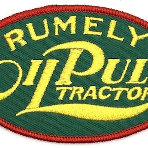 Puede incluir: Parche bordado con las palabras "RUMELY OIL PULL TRACTOR" en hilo amarillo sobre un fondo ovalado verde. El óvalo está delineado con un borde rojo.