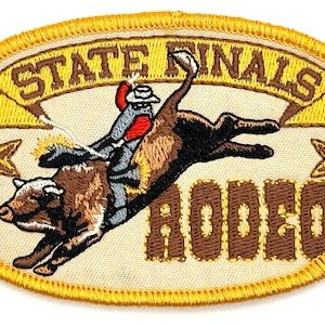 May include: An embroidered patch featuring a cowboy riding a bucking bull. The patch is oval shaped with a yellow border and a white background. The text "STATE FINALS RODEO" is embroidered in brown on the patch.
