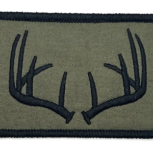 May include: A green fabric patch with a black embroidered design of a deer's antlers.