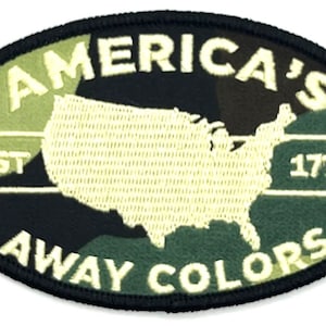 May include: A black and green oval patch with white embroidered text. The text reads "America's Est 1776 Away Colors" and features a white outline of the United States.