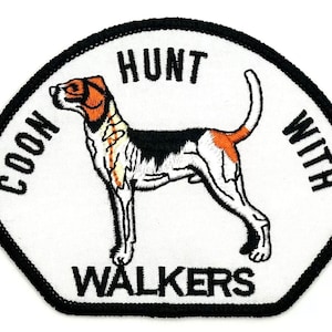 May include: White embroidered patch with a black border. The patch features a black and white hound dog with brown and orange markings. The text "COON HUNT WITH WALKERS" is embroidered in black around the dog.