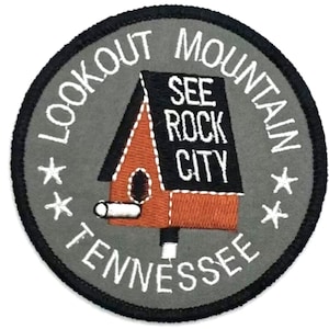 May include: A gray and white embroidered patch with a black outline. The patch features a stylized house with a chimney and the text "See Rock City" on the front. The text "Lookout Mountain Tennessee" is written in a circle around the house.