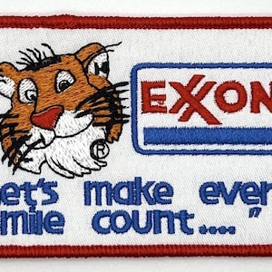 May include: Embroidered patch featuring a cartoon tiger head and the Exxon logo. The patch has a white background with a red border and the text "Let's make every mile count..." in blue.
