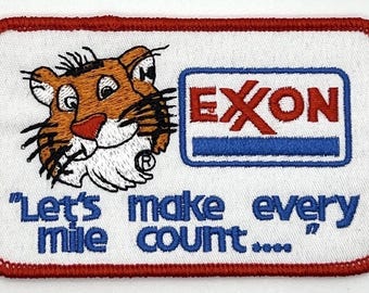 May include: Embroidered patch featuring a cartoon tiger head and the Exxon logo. The patch has a white background with a red border and the text "Let's make every mile count..." in blue.