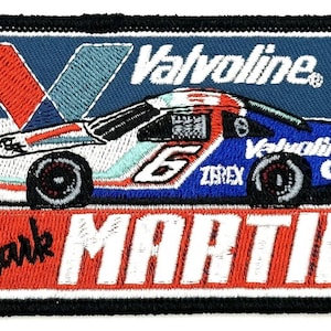 Può includere: Una toppa ricamata con una macchina da corsa bianca con accenti blu e rossi. La macchina ha il numero "6" sul lato e le parole "Valvoline" e "Zerex" su di essa. La toppa ha anche le parole "Valvoline" e "Mark Martin" su di essa.