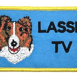 May include: Embroidered patch featuring a collie dog's face with brown, white, and black details. The patch has the words "LASSIE TV" in black text on a light blue background, with a gold border.