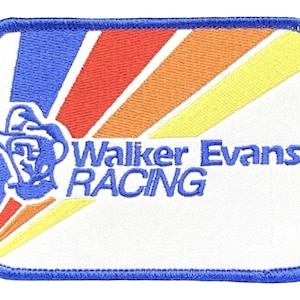 Peut inclure: Un écusson brodé blanc avec une bordure bleue. L'écusson présente un motif de soleil stylisé en orange, jaune et rouge. Le texte "Walker Evans Racing" est brodé en bleu sous le soleil.