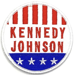 Può includere: Una toppa circolare bianca con strisce rosse e blu e stelle. Il testo "KENNEDY JOHNSON" è ricamato in rosso.
