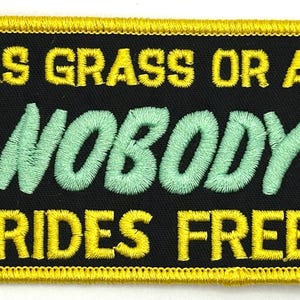Puede incluir: Un parche bordado negro y amarillo con el texto "Gas Grass or Ass Nobody Rides Free". El parche presenta dos figuras verdes a cada lado del texto.