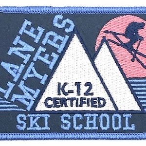 May include: Blue and white embroidered patch with the text "ilane myers k-12 certified ski school" and a graphic of a skier on a mountain with a pink sun.