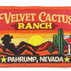Könnte beinhalten: Gestickter Aufnäher mit einer Wüstenlandschaft, einer liegenden Silhouette, einem Kaktus und einem Cocktail. Der Aufnäher trägt den Text "Velvet Cactus Ranch, Pahrump, Nevada" in Gelb und Weiß vor einem Sonnenuntergangshintergrund.
