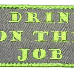May include: A gray fabric patch with green stitching around the edges. The text "I DRINK ON THE JOB" is embroidered in green.