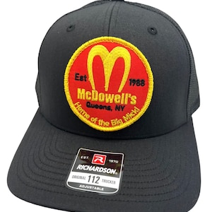 May include: Black trucker hat with a red and yellow embroidered patch that says "Est. 1988 McDowell's Queens, NY Home of the Big Mickl". The hat also has a black and white label that says "EST. 1970 RICHARDSON ORIGINAL 112 TRUCKER ADJUSTABLE".