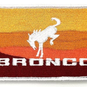 May include: A white embroidered patch featuring a bucking bronco silhouette against a sunset backdrop. The word "BRONCO" is displayed beneath the horse.