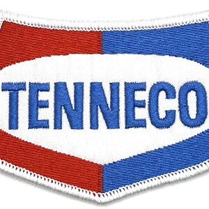 Può includere: Una toppa ovale bianca con un logo ricamato in blu che dice "TENNECO". L'ovale è circondato da un bordo bianco e uno sfondo rosso e blu.