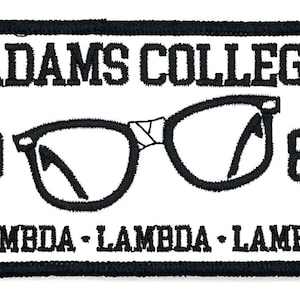Peut inclure: Écusson brodé noir et blanc avec le texte "Adams College" et les années "1984". L'écusson présente également une paire de lunettes et le texte "Lambda - Lambda - Lambda".