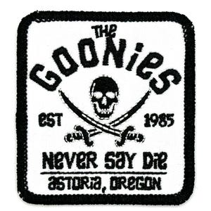 Può includere: Toppa ricamata in bianco e nero con il testo "The Goonies Est. 1985 Never Say Die Astoria, Oregon" e un teschio e ossa incrociate.