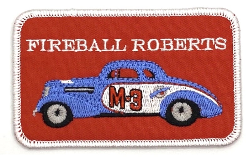 Puede incluir: Parche bordado con un dise&ntilde;o de coche de carreras vintage. El parche tiene un fondo rojo con las palabras "FIREBALL ROBERTS" en blanco. El coche es azul y blanco con el n&uacute;mero "M-3".