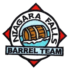 May include: White and red embroidered patch with a compass design. The center of the patch features a brown barrel floating in blue water. The text "NIAGARA FALLS BARREL TEAM" is written in black on a white banner.
