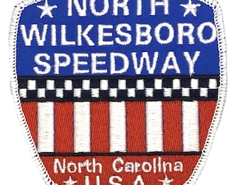 May include: A white embroidered patch with a blue background. The patch says "North Wilkesboro Speedway" with a star on either side of the text. Below the text is a checkered flag design and a red and white striped design. The bottom of the patch says "North Carolina" and "U.S.A." with a star on either side of the text.