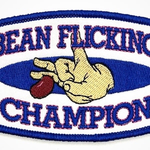 May include: A white embroidered patch with blue and pink stitching. The patch features a hand holding a red bean and the text "BEAN FLICKING CHAMPION".