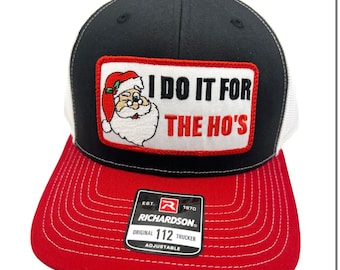 May include: Black and white trucker hat with a red bill. The hat has a white mesh back and a red, white, and black patch that says "I DO IT FOR THE HO'S" with a cartoon Santa Claus on it. The hat also has a black label with white text that says "EST. R 1970 RICHARDSON® ORIGINAL 112 TRUCKER ADJUSTABLE".