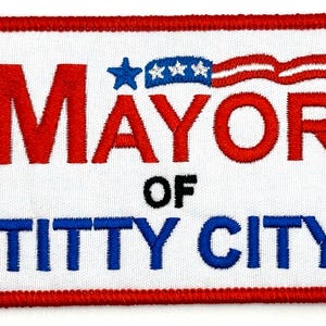 Può includere: Una toppa ricamata bianca con accenti rossi e blu. La toppa recita "Mayor of Titty City" con una piccola bandiera americana sopra la parola "Mayor".