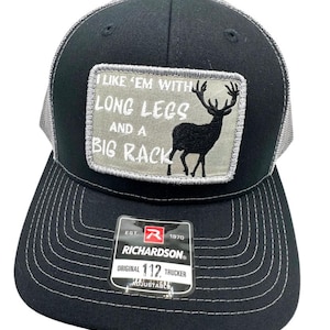 May include: Black and grey trucker hat with a patch that says "I like 'em with long legs and a big rack" and a silhouette of a deer. The hat is adjustable and has the Richardson logo.