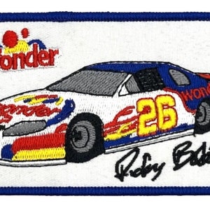 May include: White race car with blue, red, and yellow flames and the number 26 on the side. The car has the word "Wonder" on the side and the driver's signature "Ricky Bobby" below the car.
