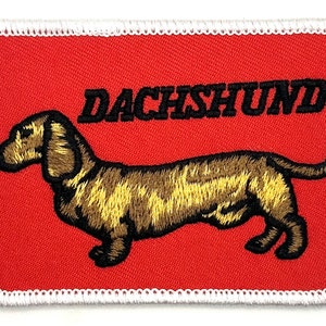 May include: Embroidered patch with a brown dachshund on a red background. The text "DACHSHUND" is above the dog.