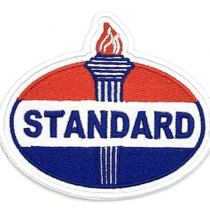 Puede incluir: Parche bordado con la palabra "STANDARD" en azul sobre fondo blanco, dentro de un óvalo rojo y azul. Una antorcha con una llama en la parte superior. El parche tiene un borde blanco.