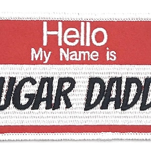 May include: A red and white name tag with the text "Hello My Name is SUGAR DADDY" in black.