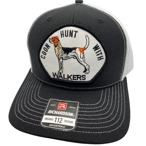 May include: Black and white trucker hat with a white patch featuring a hound dog and the text "Coon Hunt With Walkers". The hat has a white mesh back and a black front with a white stitched brim. The hat has a black label with the text "Richardson" and "Original 112 Trucker Adjustable".