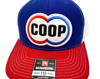 May include: A blue, red, and white trucker hat with a white circle with the word "COOP" in black letters inside. The hat is made by Richardson 112 and is adjustable.