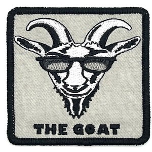 Puede incluir: Un parche bordado blanco con una cabra que lleva gafas de sol y el texto "THE GOAT" debajo. El parche tiene un borde negro.