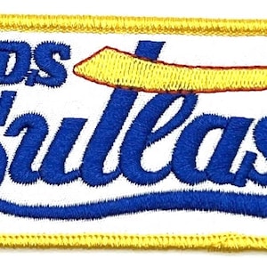 May include: A yellow and red embroidered patch with the text "OLDS CULLASS" in blue lettering. A yellow sword with a red handle is above the text.
