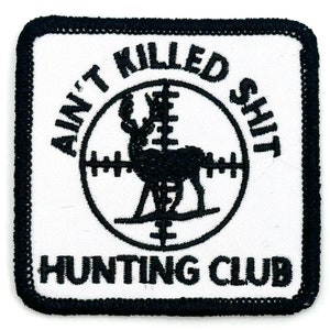 Może przedstawiać: Biały kwadratowy znaczek z czarnym haftowanym tekstem i sylwetką jelenia w tarczy. Tekst brzmi "Ain't Killed Shit Hunting Club".