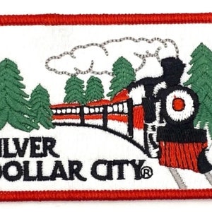 May include: Embroidered patch featuring a train, pine trees, and the text "Silver Dollar City" in black. The patch has a red border and a white background. The train is red, black, and white.